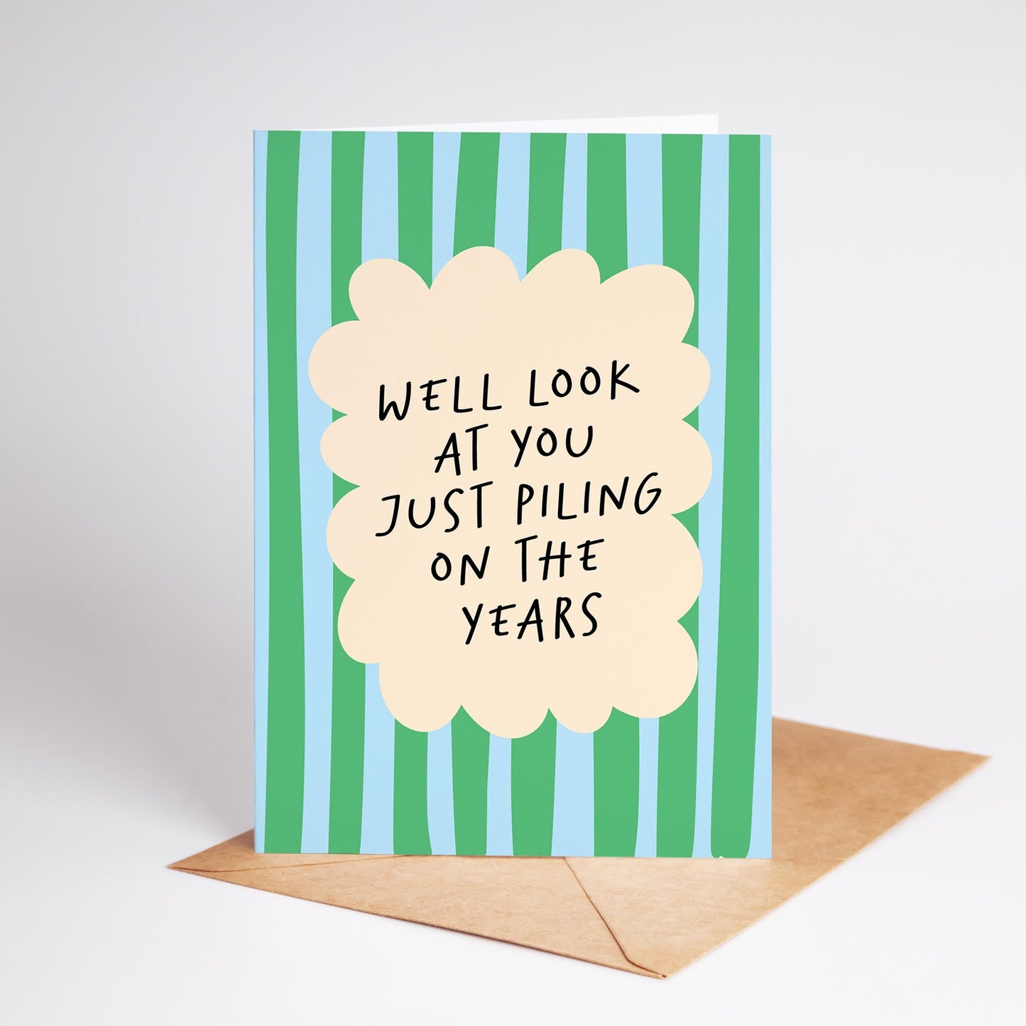 Card with green and blue striped background and humorous text, with a beige envelope.