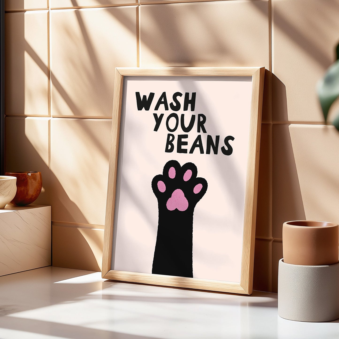 Framed poster with paw print and 'Wash Your Beans' text on a tiled wall.