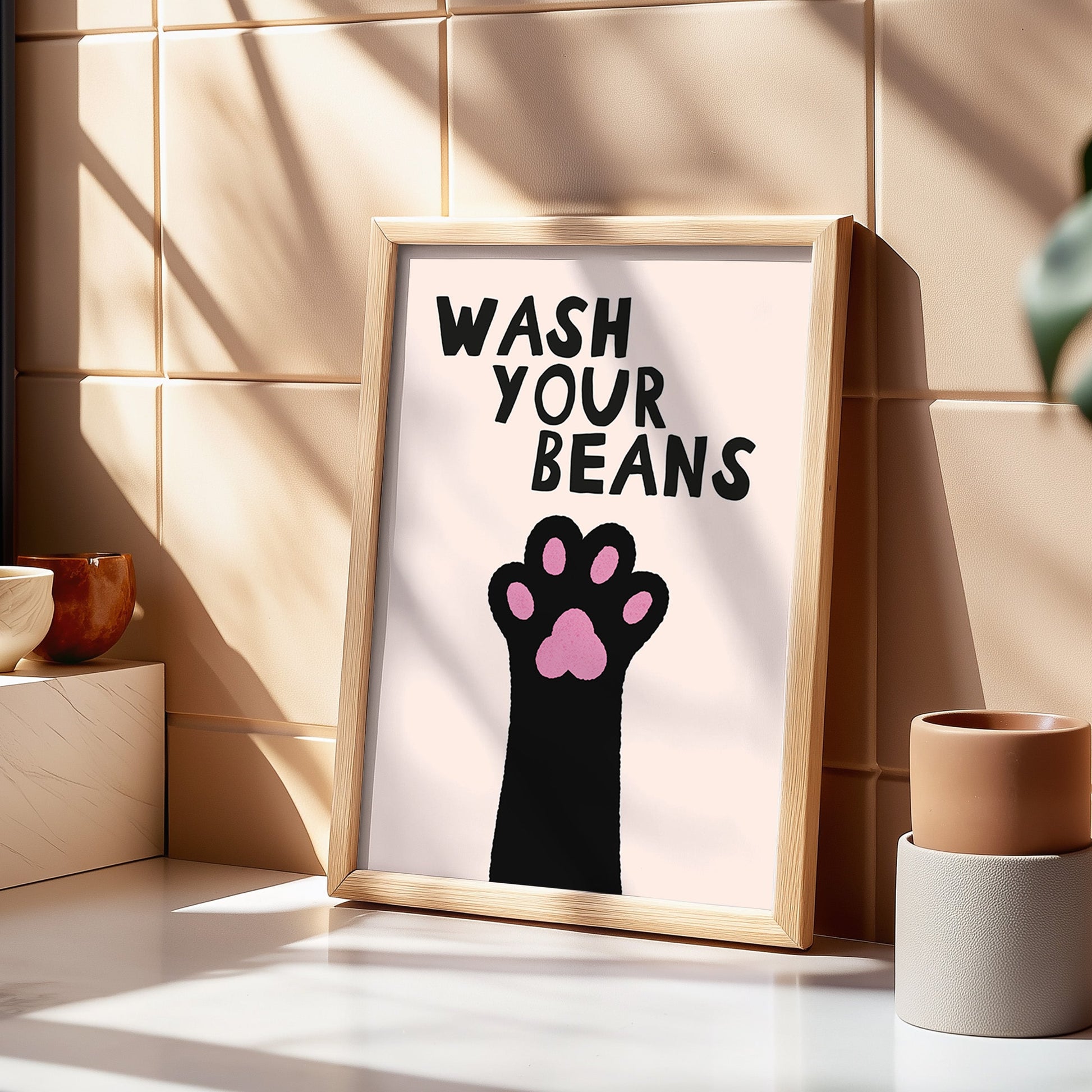 Framed poster with paw print and 'Wash Your Beans' text on a tiled wall.